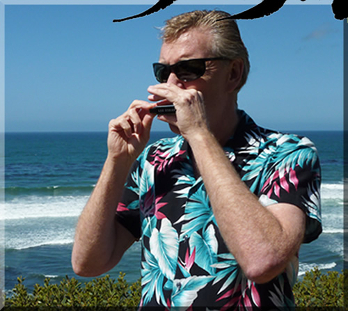 Photo of Jerry Michelsen playing harmonica in a Hawaiian shirt on a cliff overlooking the ocean
